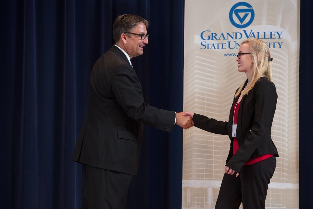 Doctor Smart shaking hands with an award recipient in a black blazer and red shirt